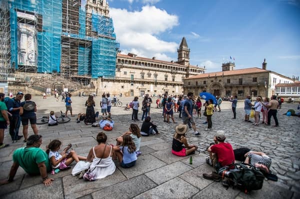 Vários peregrinos sentados na praça do Obradoiro, em Santiago de Compostela, na frente da Catedral